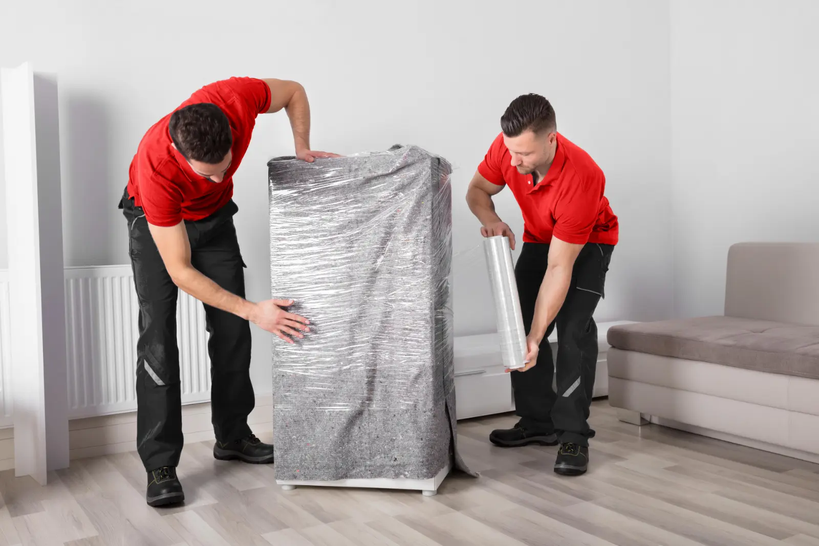 Two Desert Moving movers wrapping a tall appliance in protective wrap