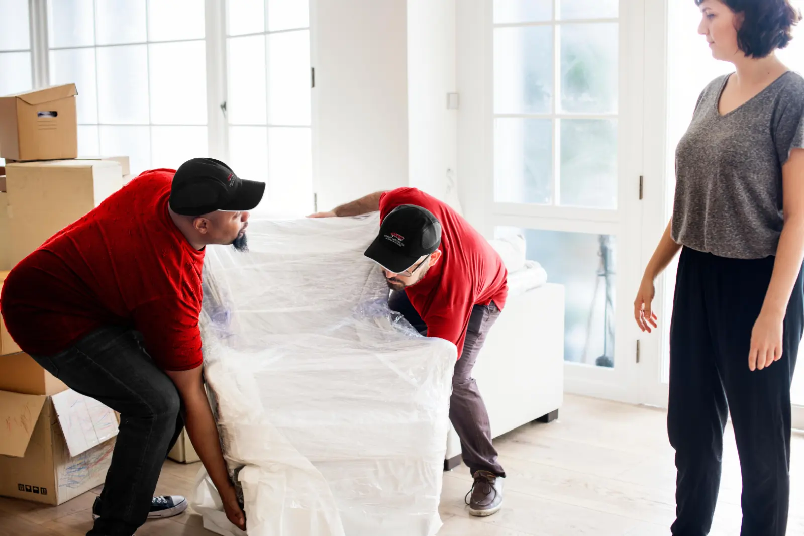 Two Desert Moving movers wrapping a white sofa in plastic while the homeowner watches